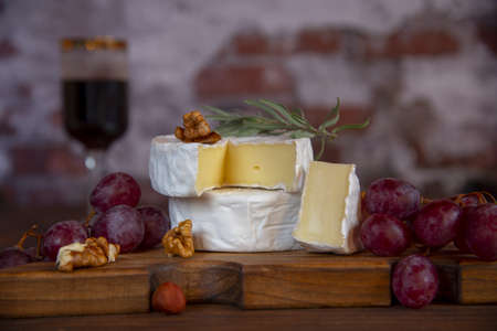 Cheese with white mold, nuts and grapes on a wooden cutting board. Food background.の写真素材