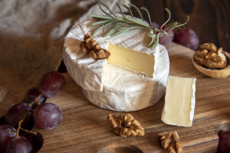 Cheese with white mold, nuts and grapes on a wooden cutting board. Food background.の写真素材