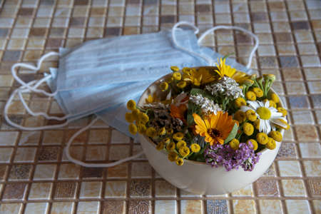 A ceramic bowl with medicinal herbs and a protective medical disposable mask on the countertop.の写真素材