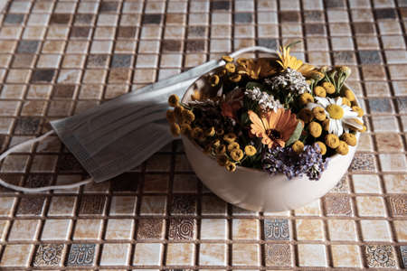 A ceramic bowl with medicinal herbs and a protective medical disposable mask on the countertop.の写真素材