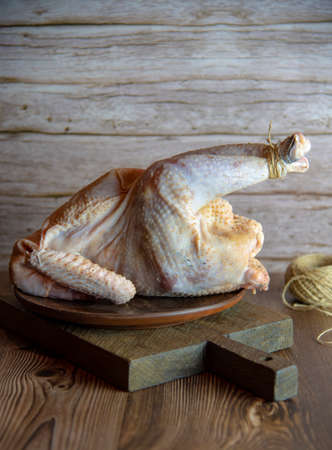 Fresh raw meat. A pale chicken carcass with its legs tied lies on a ceramic dish on a wooden cutting board.の写真素材