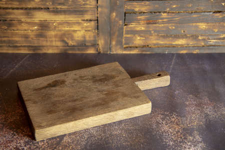 A wooden old kitchen cutting board lies on the table on a wooden background.の写真素材