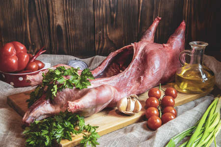 Fresh raw meat. Nutria carcass on a wooden cutting board with fresh vegetables and herbs.の写真素材