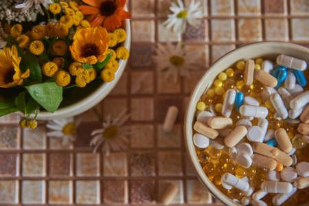 A ceramic bowl with medicinal herbs and a bowl with various pills and tablets are on the countertop.Focus on flowers.の写真素材