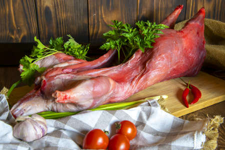 Fresh raw meat. Nutria carcass on a wooden cutting board with fresh vegetables and herbs.の写真素材