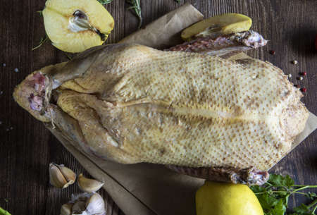 Fresh raw meat. A duck carcass with vegetables, herbs and spices lies on a sheet of parchment paper on a wooden background.の写真素材