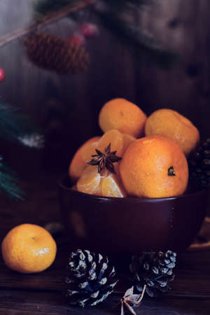 Juicy fresh tangerines lie in a brown ceramic bowl. Fir branches in the background.の写真素材