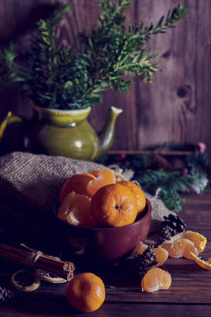 Juicy fresh tangerines lie in a brown ceramic bowl. Fir branches in the background.の写真素材