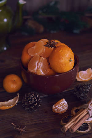 Juicy fresh tangerines lie in a brown ceramic bowl. Fir branches in the background.の写真素材