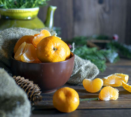 Juicy fresh tangerines lie in a brown ceramic bowl. Fir branches in the background.の写真素材