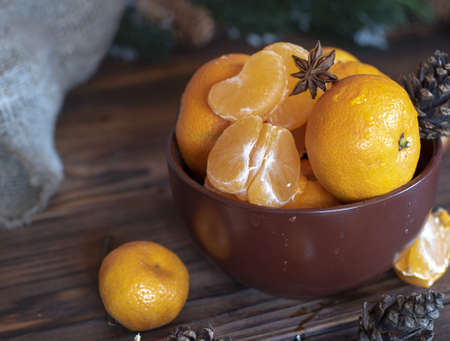 Ripe bright tangerines in a brown ceramic bowl, pine cones and fragrant spices lie nearby. New Year's traditional background.の写真素材