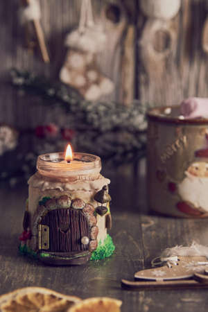 A burning handmade candle on the background of Christmas decor and mugs with cocoa and marshmallows.の写真素材