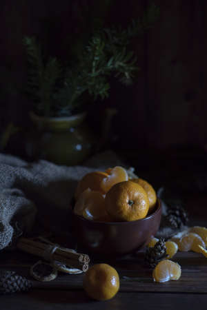 Juicy fresh tangerines lie in a brown ceramic bowl. Fir branches in the background.の写真素材