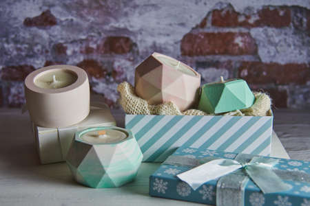 Several colorful handmade soy wax candles in ceramic candlesticks in a Christmas gift box on a brick wall background.の写真素材