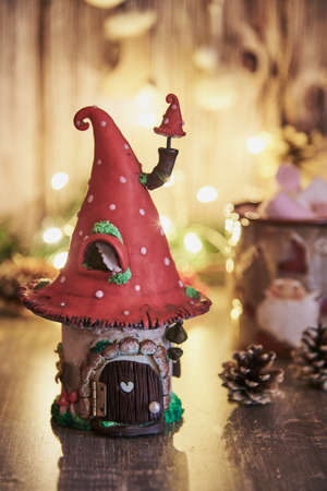 Handmade clay house with a roof in the shape of a fly agaric on the background of a glowing garland and Christmas decor.の写真素材
