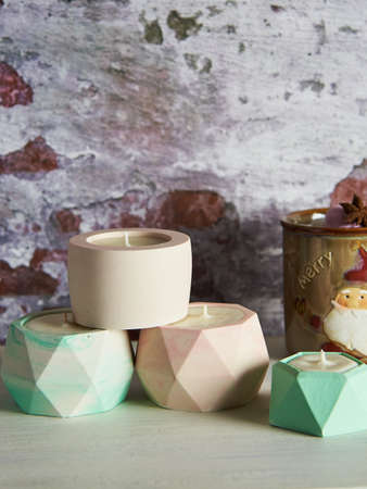 Several colorful handmade soy wax candles in ceramic candlesticks on a brick wall background.の写真素材