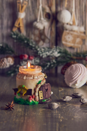 A burning handmade candle on the background of Christmas decor and mugs with cocoa and marshmallows.の写真素材