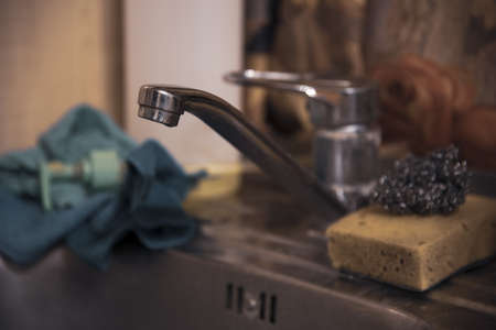 The water tap over the kitchen sink with dirty dishes. Focus on the front of the faucet.の写真素材