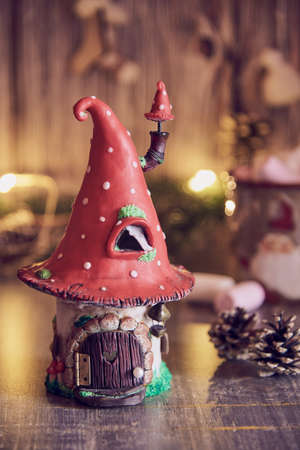 Handmade clay house with a roof in the shape of a fly agaric on the background of a glowing garland and Christmas decor.の写真素材