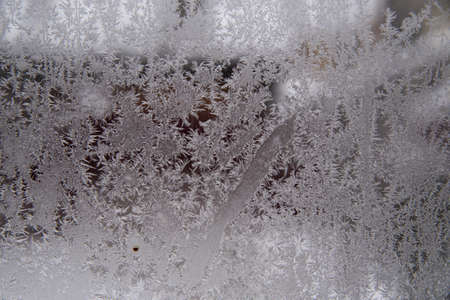 Frosty pattern on dirty window glass on a cloudy winter day. Abstract background.