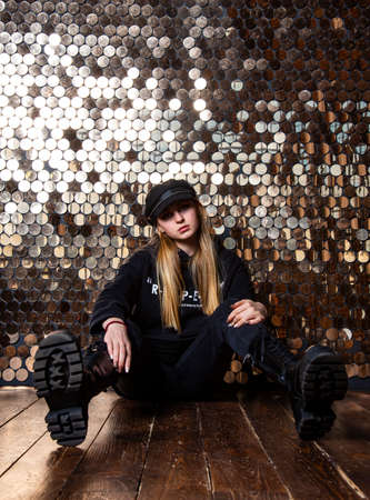 A teenage girl with blonde hair in black clothes is sitting by a golden wall.の写真素材