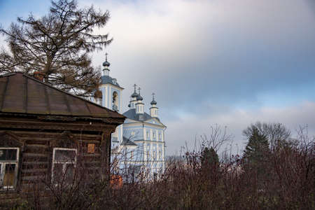 An old wooden dilapidated house on the background of a beautiful blue church.