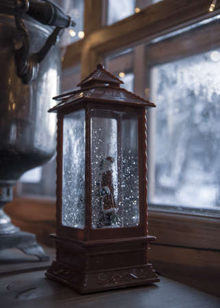 A Christmas lantern and an ancient samovar on a wooden table against the background of a window.