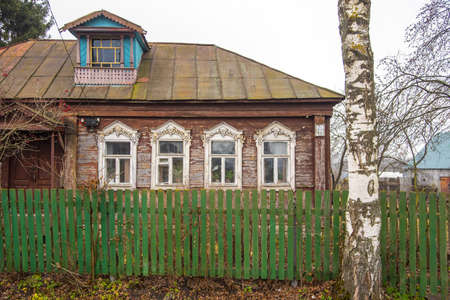 An old wooden village house behind a fence on a cloudy autumn day.の写真素材