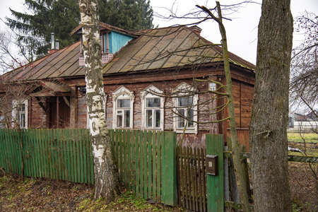 An old wooden village house behind a fence on a cloudy autumn day.の写真素材