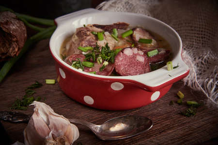 A bright ceramic bowl of soup with smoked sausage on a wooden table. food background.の写真素材