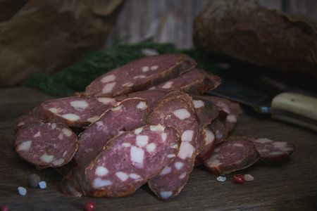 Smoked sausage, cut into pieces, sprinkled with spices, lies on a wooden cutting board. food background.の写真素材