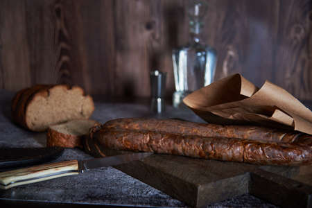 food background. Still life with a hunting sausage decanter and a hunting knife. Sausage on a cutting board.の写真素材