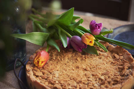 Homemade cake sprinkled with cookie crumbs on a metal vintage dish, decorated with tulips. Food background.の写真素材