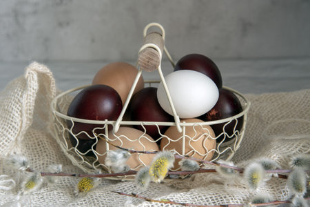 Easter colored eggs and natural eggs lie in a small basket decorated with willow branches.の写真素材