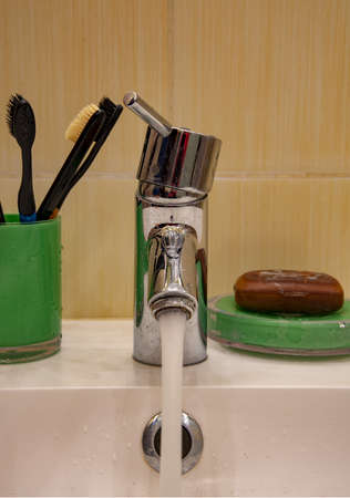 A metal faucet with running water, toothbrushes and brown tar soap in the bathroom.の写真素材