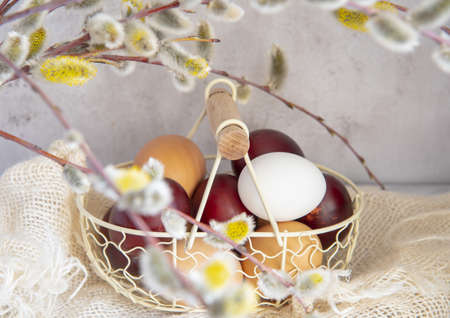 Easter colored eggs and natural eggs lie in a small basket decorated with willow branches.の写真素材