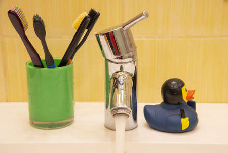 A metal faucet, toothbrushes and and a rubber duck on the sink. in the bathroom.の写真素材