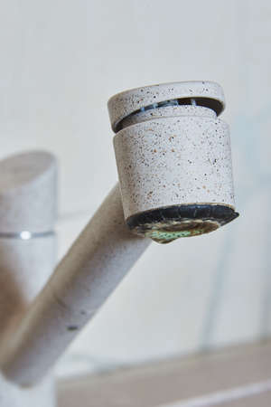 Close-up of a beige faucet with a drop of water on the background of the wall.