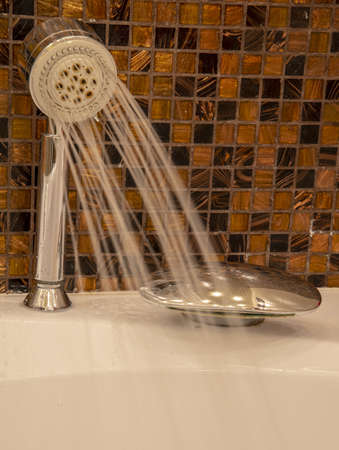 A shower head with running water and an oval-shaped faucet in the bathroom against a brown wall.