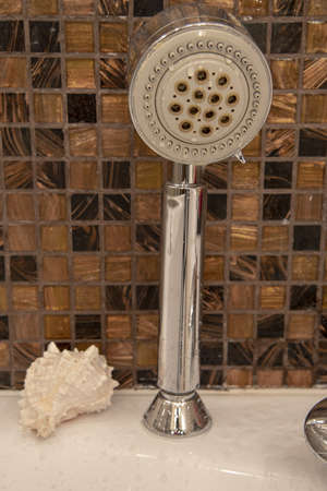 A Shower watering can with water drops, a seashell in the bathroom against the background of a wall of small tiles.の写真素材