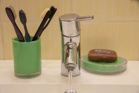 A metal faucet with running water, toothbrushes and brown tar soap in the bathroom.の写真素材