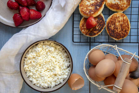 Cottage cheese, eggs, strawberries and cheesecakes on a blue countertop. Top view, food background.の写真素材