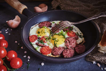 Fried eggs with smoked sausage, tomatoes and herbs in a frying pan.の写真素材