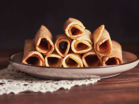 Waffle tubes on a ceramic plate on a wooden table. food background.の写真素材