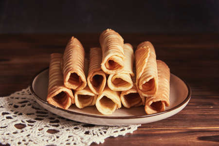 Waffle tubes on a ceramic plate on a wooden table. food background.の写真素材