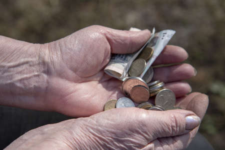 Small coins and a 50 ruble bill in the wrinkled hands of an elderly woman.の写真素材