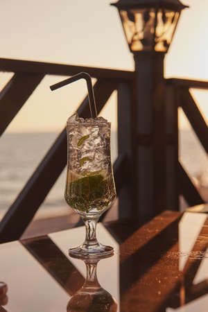 A glass with a cold refreshing drink on a glass table against the sunset background.の写真素材