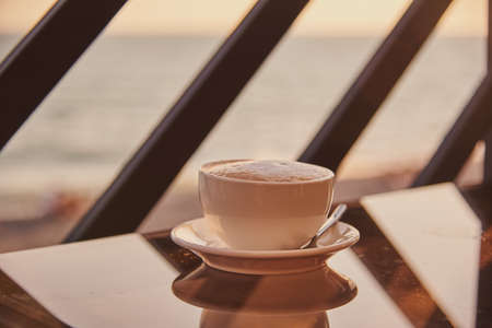 A cup of cappuccino on a glass table against the sunset.の写真素材