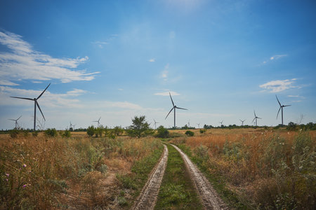 Dirt road in fields where there are large wind turbines.の写真素材