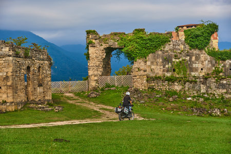 Abkhazia, the village of Agubedia, the Bedia Cathedral, August 2022. A man on a motorcycle rides along a dirt road among green grass to the ruins of an ancient Bedia temple.のeditorial素材